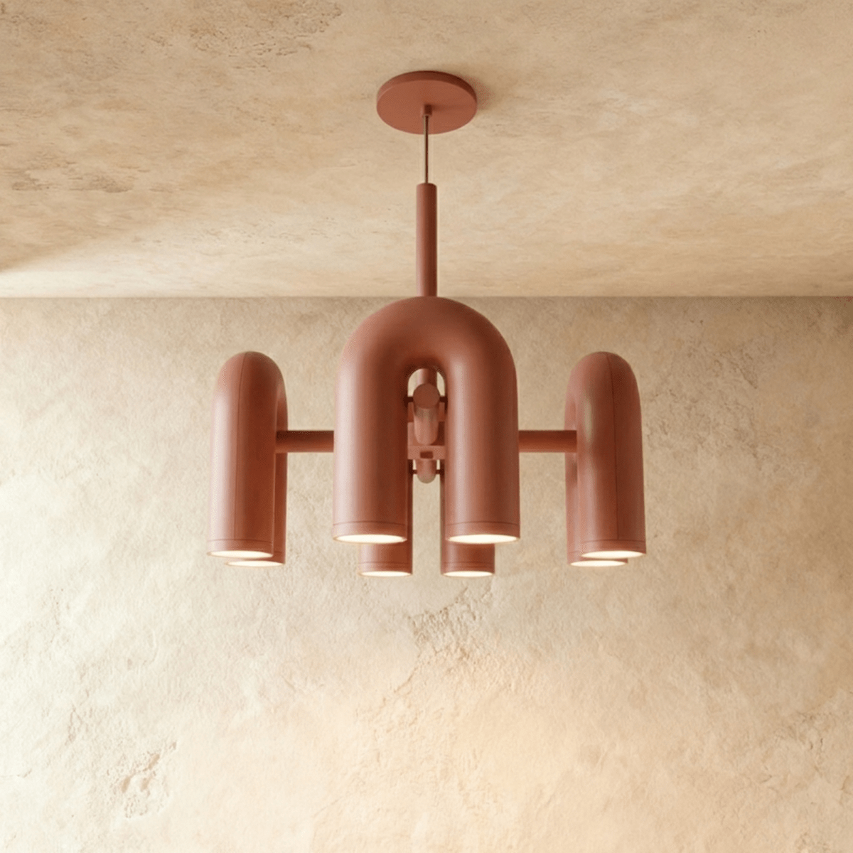 Clérachic chandelier of rounded U-shaped modules in terracotta orange, lit from below against a limewashed plaster wall.