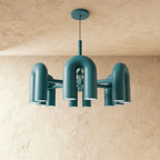 Clérachic larger chandelier with a fuller ring of blue U-shaped arch modules, hung on a cable against a plaster wall.