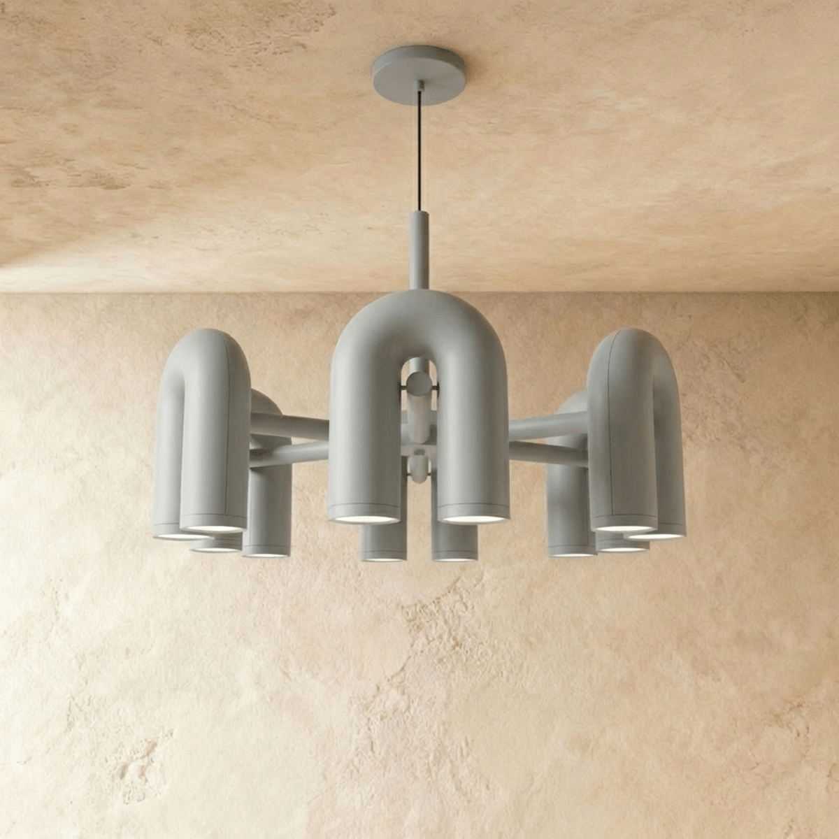 Clérachic larger chandelier with a fuller ring of light grey U-shaped arch modules, hung on a cable against a plaster wall.