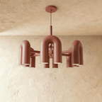 Clérachic larger chandelier with a fuller ring of terracotta orange U-shaped arch modules, hung on a cable against plaster.