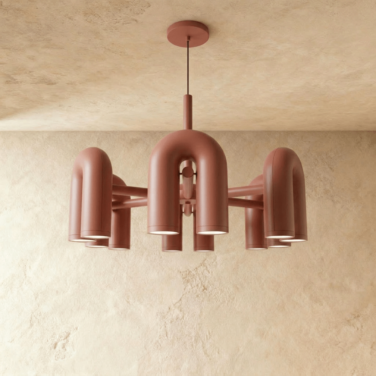 Clérachic larger chandelier with a fuller ring of terracotta orange U-shaped arch modules, hung on a cable against plaster.