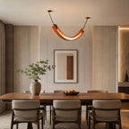 A Clérachic U-shaped pendant with a warm light strip hangs over a walnut dining table, in front of a framed print and a vase of stems.