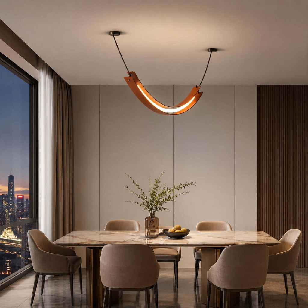 Lit Clérachic U-shaped pendant over a marble-top dining table with rounded chairs, with a night city view through a tall window.
