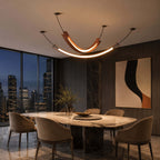 A Clérachic pendant with a terracotta U-shaped curve, and a longer slim strip light beneath it, over a stone table at dusk.
