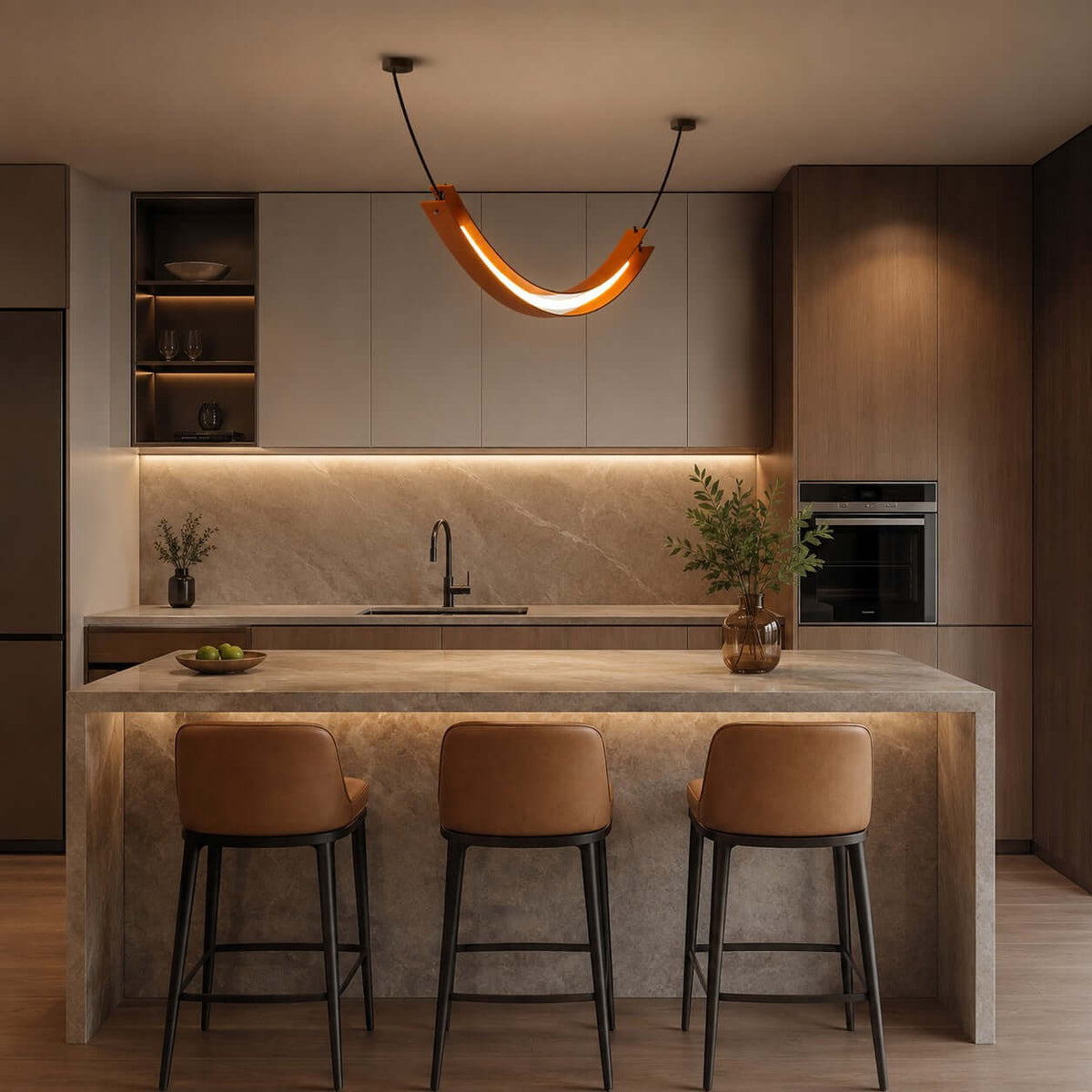 This Clérachic U-shaped pendant glows warm above a stone kitchen island with three tan leather stools and a lit splashback.