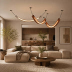 Several Clérachic curved pendants hang over an open living room with a cream sectional, a round wooden coffee table and a kitchen beyond.