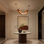 Lit terracotta U-shaped Clérachic pendant over a round fluted-base table in a hall, with a large abstract painting behind.