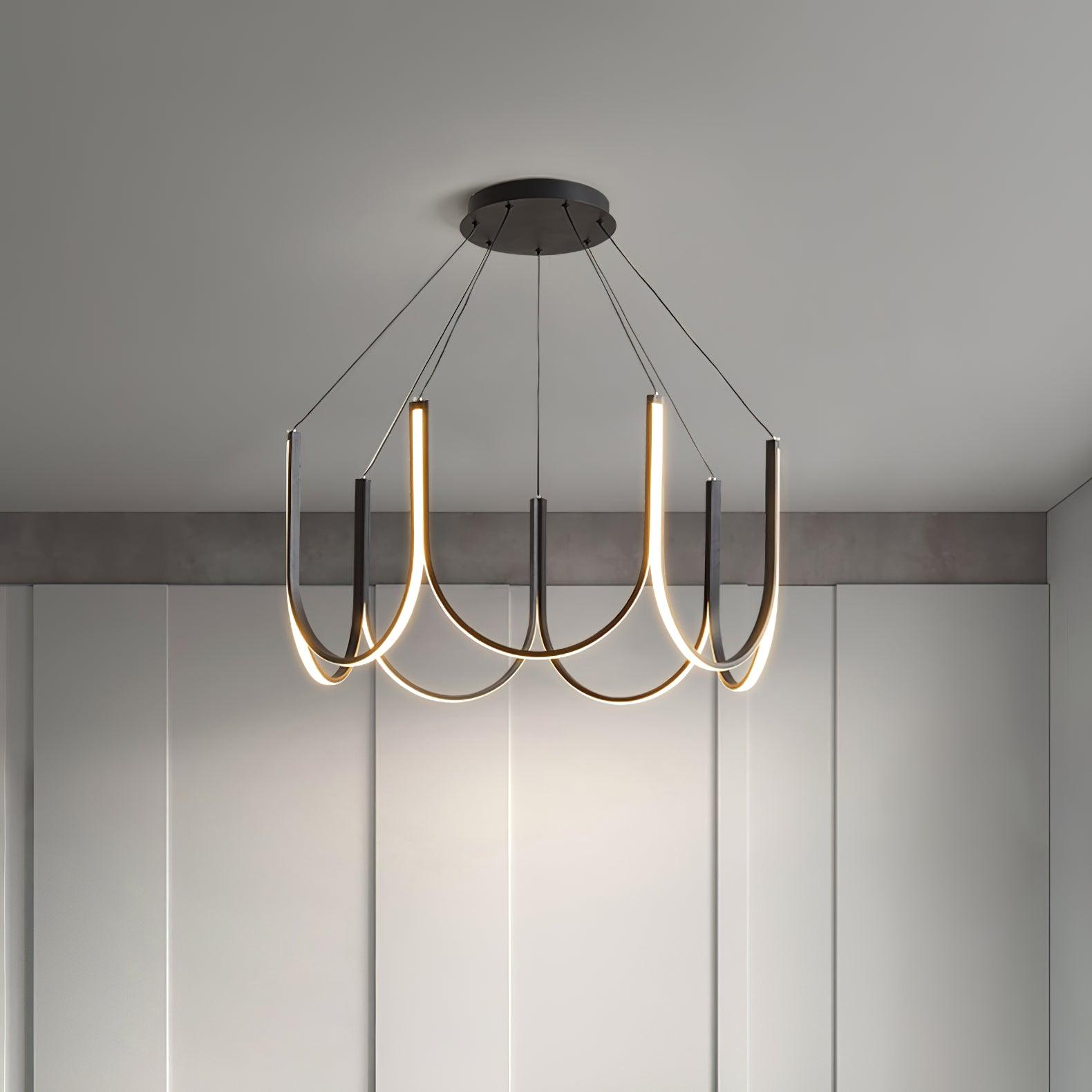 The Clérachic looped arm pendant lit above a pale room, warm light tracing each curve.