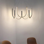 Clérachic looped arm pendant glowing in a cream corner, light washing up the wall.