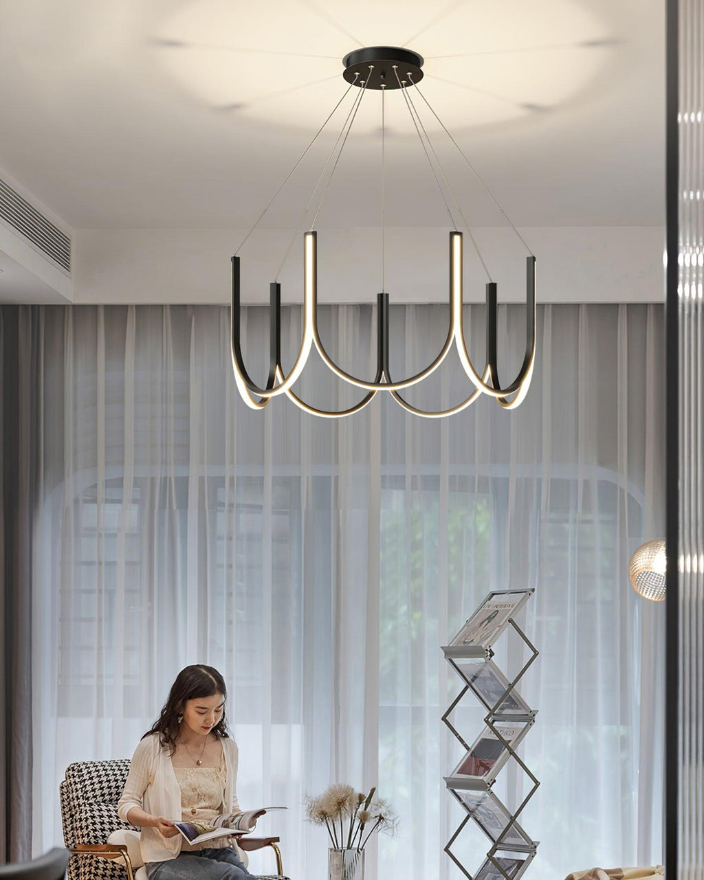 Clérachic looped arm pendant lit above a woman reading beside sheer curtains.