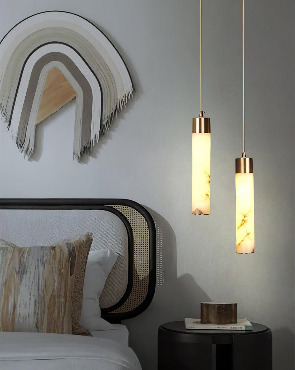 Clérachic pendants glow beside a bed at two different drops, above a black drum side table and a woven wall hanging.