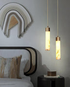 Clérachic pendants glow beside a bed at two different drops, above a black drum side table and a woven wall hanging.