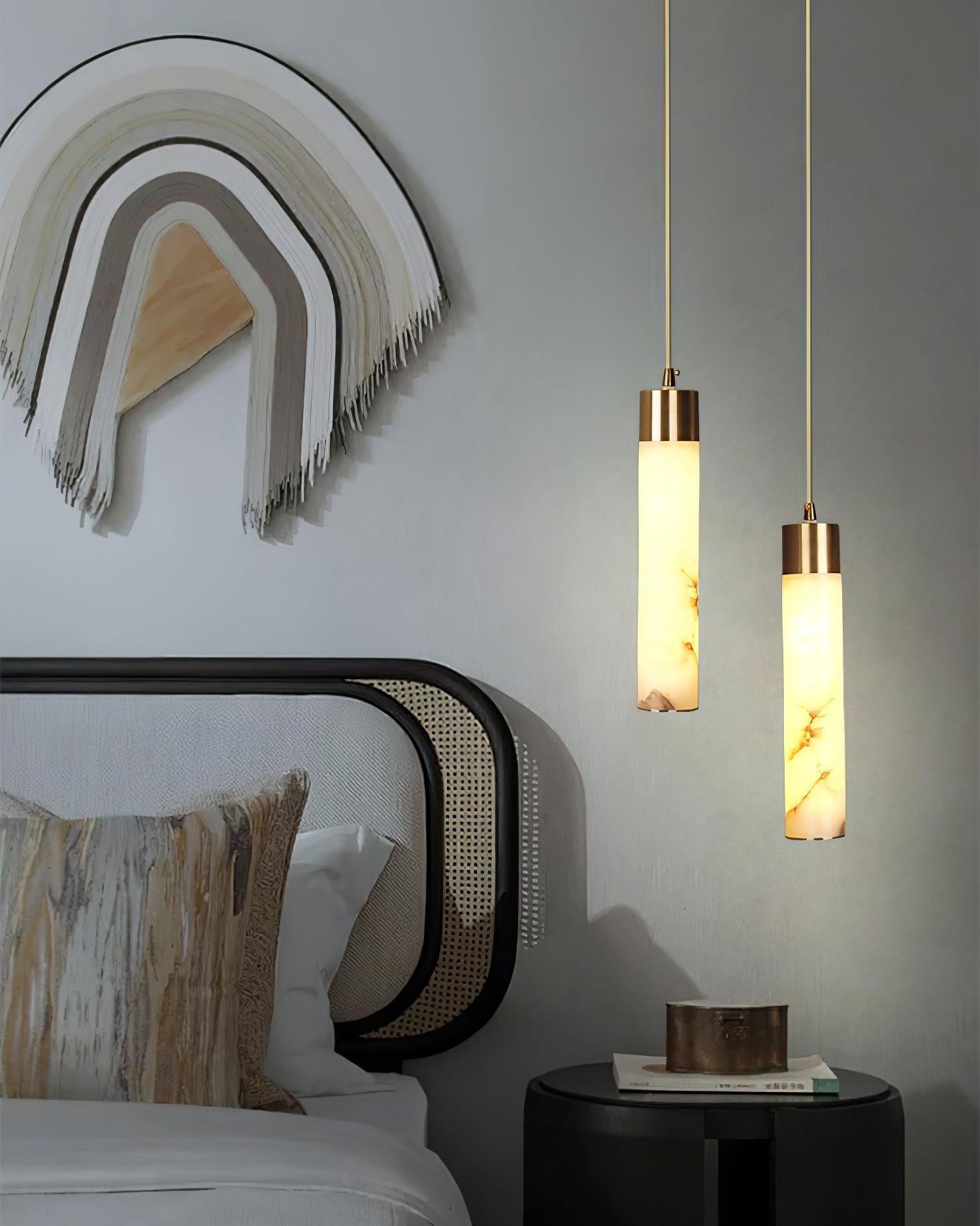 Clérachic pendants glow beside a bed at two different drops, above a black drum side table and a woven wall hanging.