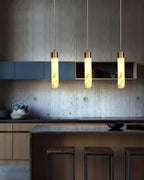The Clérachic drops light a wood and concrete kitchen island, three cylinders spaced above dark bar stools.