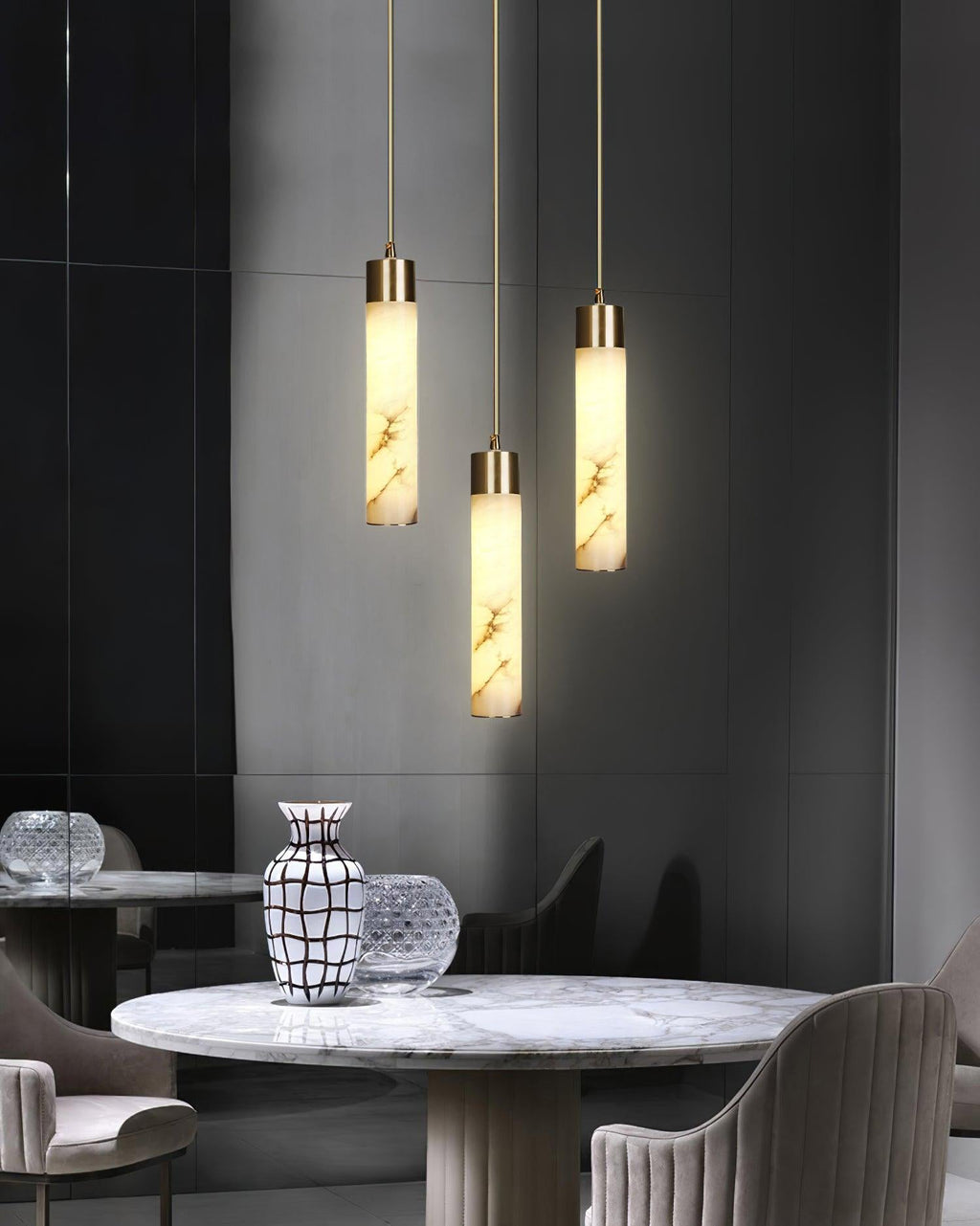 The Clérachic cylinders hang in a dark dining corner above a round marble café table and upholstered chairs.