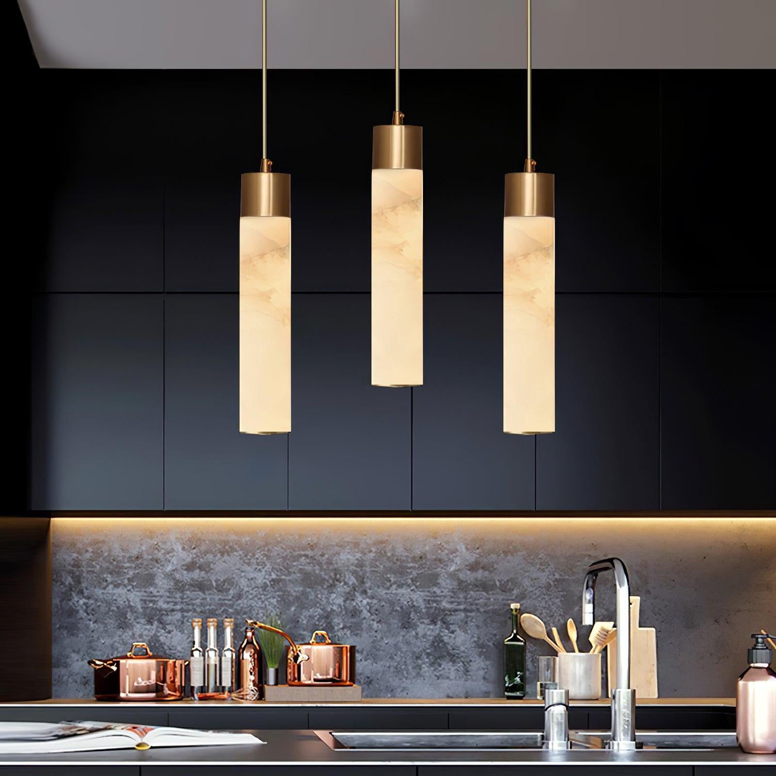 The Clérachic drops light a matte black kitchen run, copper pans and a stone splashback glowing underneath.