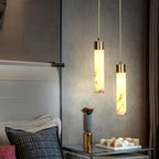 Clérachic cylinders hang over a glass bedside table, throwing warm light across a padded leather headboard.