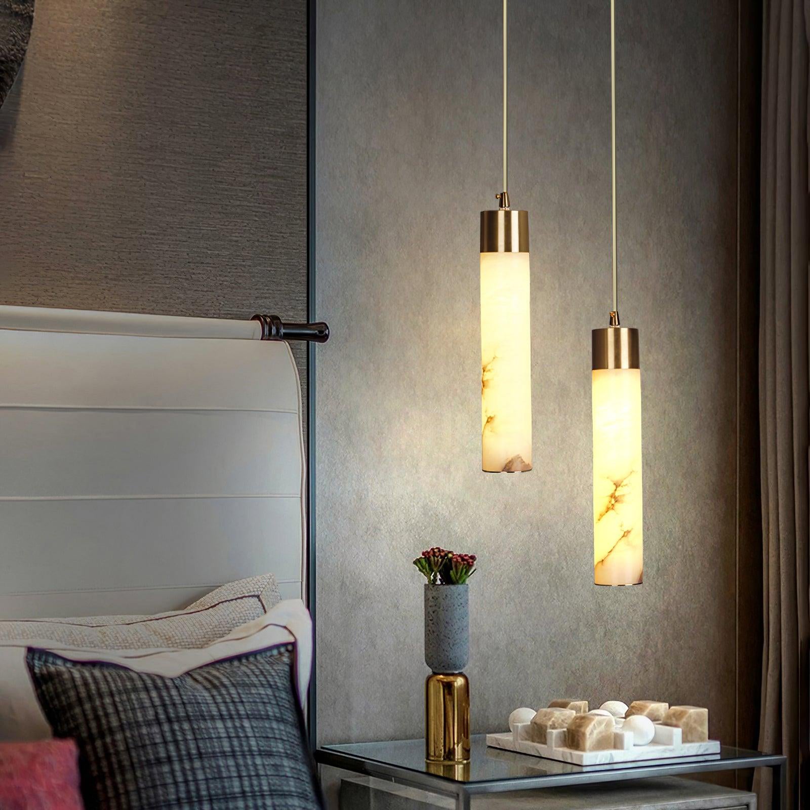 Clérachic cylinders hang over a glass bedside table, throwing warm light across a padded leather headboard.
