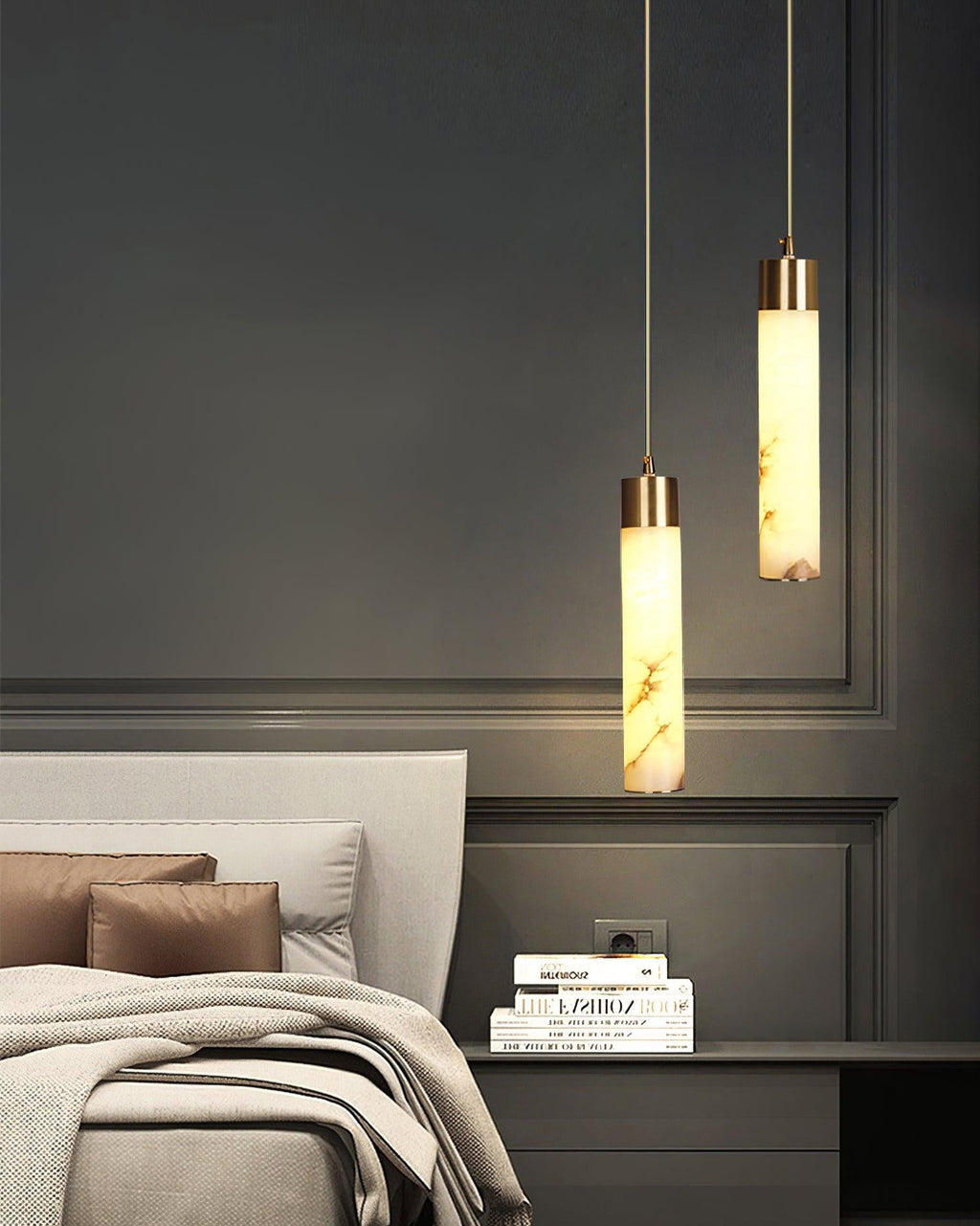 Clérachic pendants light a bedside stack of books against classic wall mouldings in a low, quiet bedroom.