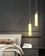 Clérachic pendants light a bedside stack of books against classic wall mouldings in a low, quiet bedroom.