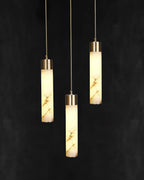 The Clérachic trio lit against near-black, each alabaster tube carrying its own pattern of grey and amber veining.