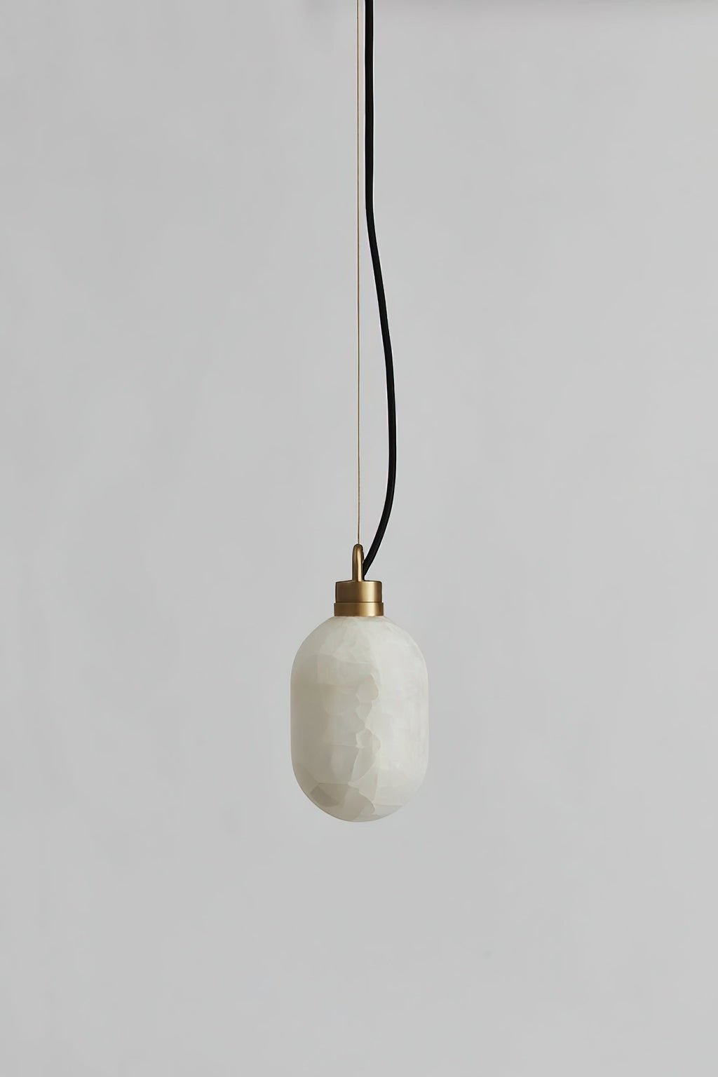 The Clérachic Eclipse pendant unlit on a grey plaster wall, showing the cool white stone shade and black flex.