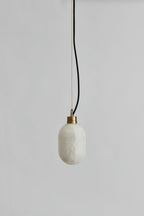 The Clérachic Eclipse pendant unlit on a grey plaster wall, showing the cool white stone shade and black flex.