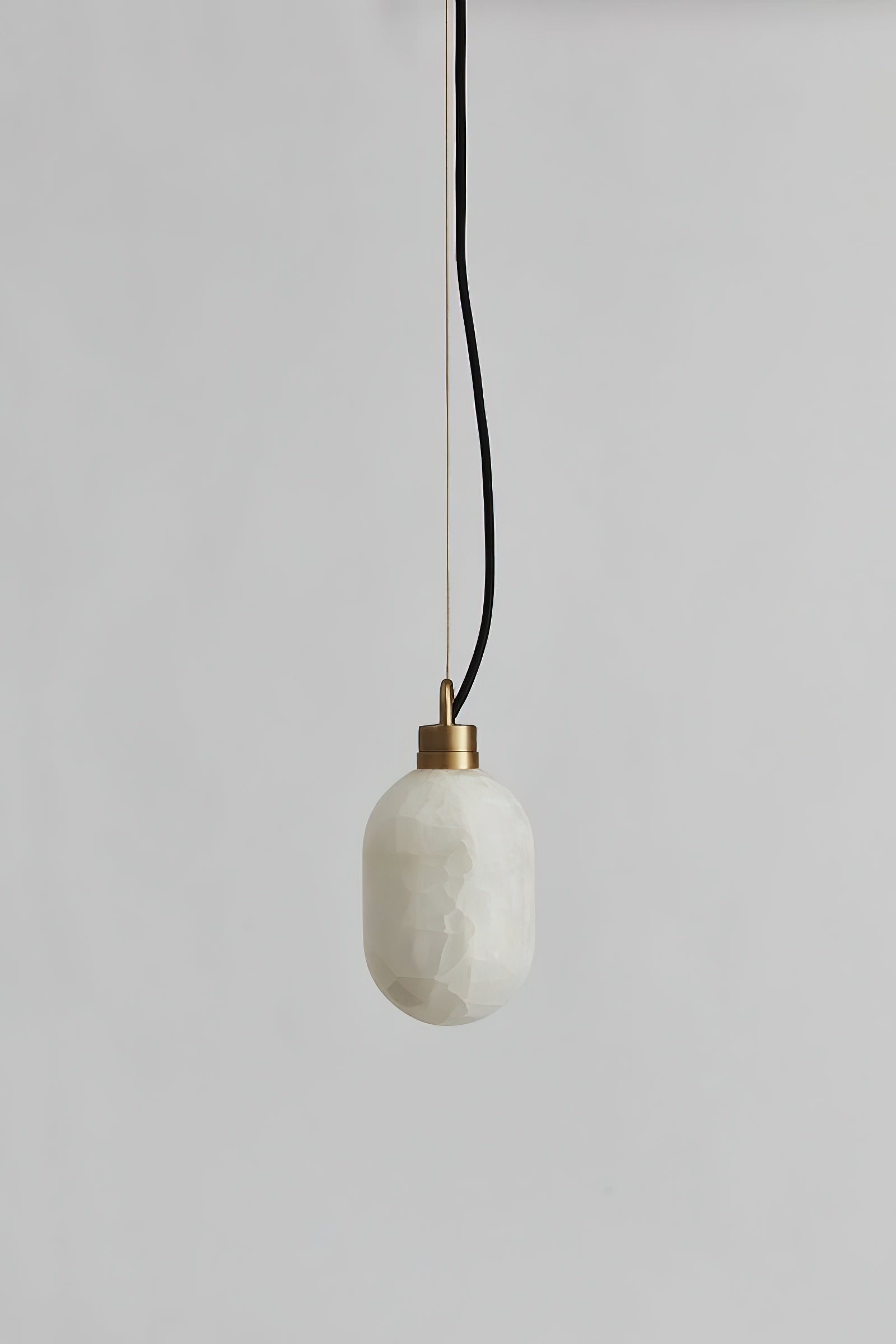 The Clérachic Eclipse pendant unlit on a grey plaster wall, showing the cool white stone shade and black flex.
