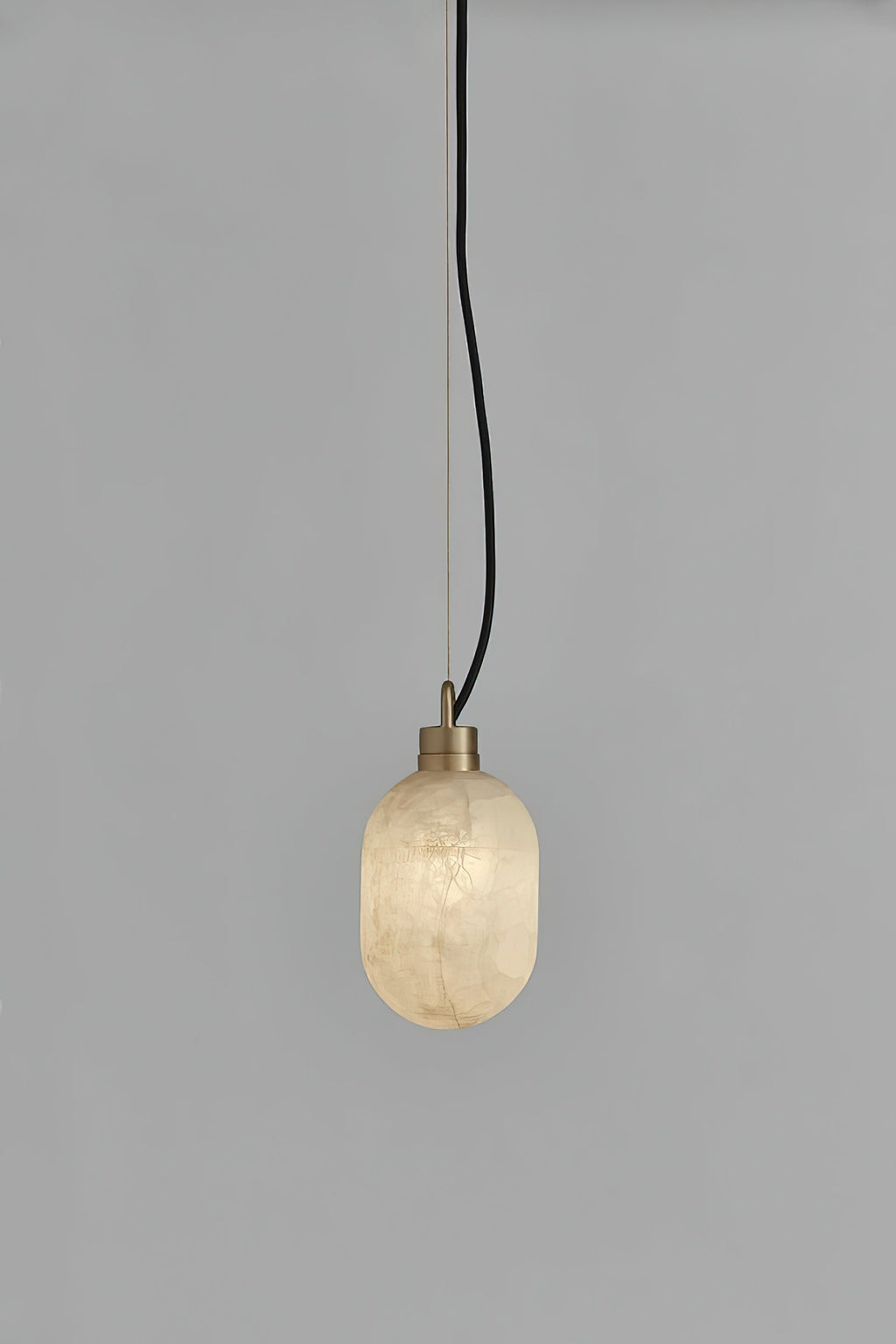 The Clérachic Eclipse pendant switched on, its alabaster capsule shade casting a soft glow against grey plaster.