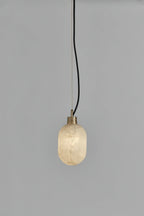 The Clérachic Eclipse pendant switched on, its alabaster capsule shade casting a soft glow against grey plaster.