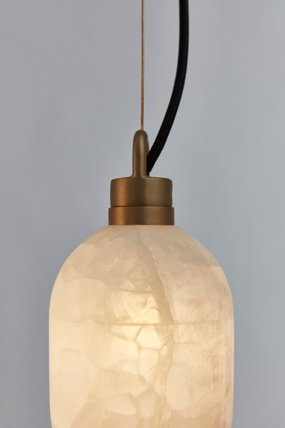 Clérachic Eclipse pendant close up, the lit alabaster shade showing its crystalline grain under the brass cap.