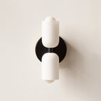 Up-and-Down Opal Wall Sconce from Clérachic in matte black, its round backplate set against a pale plaster wall.