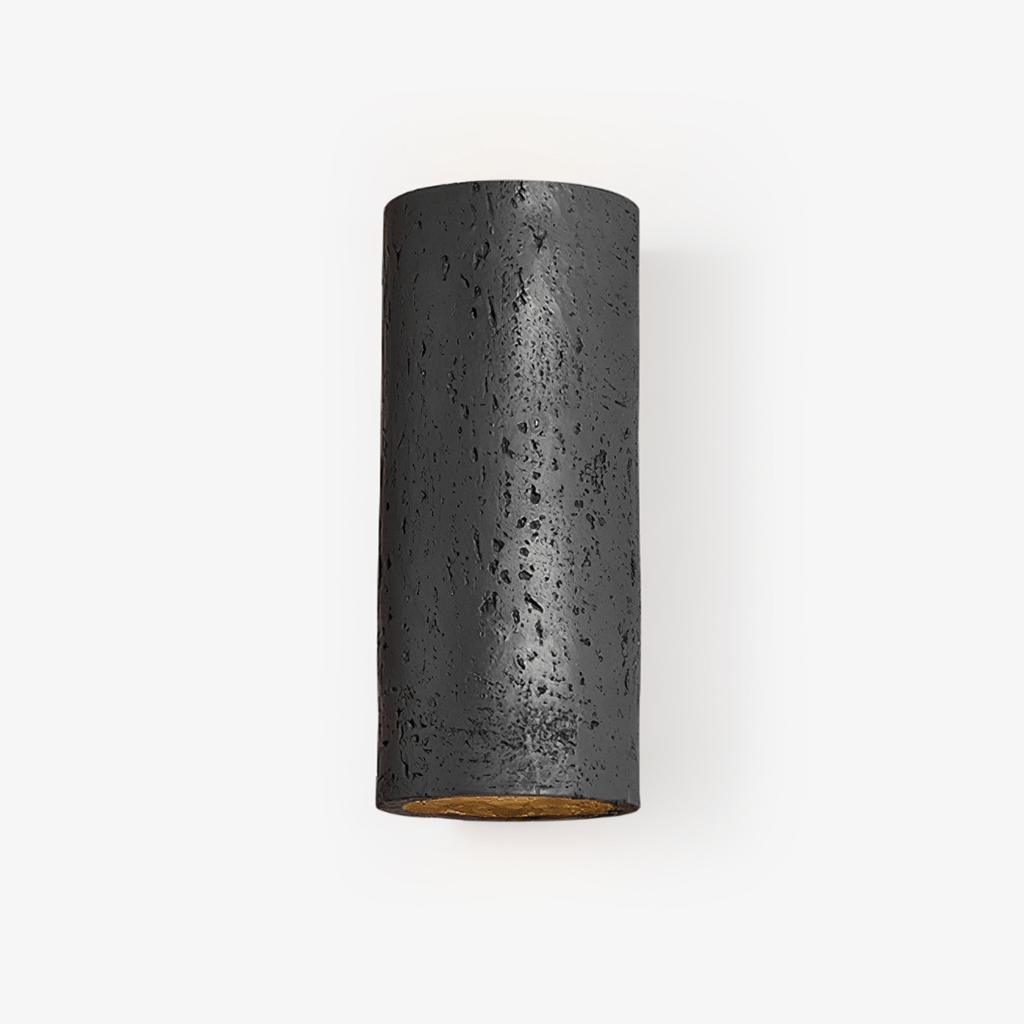 Black cylinder wall light with a pitted, stone-like surface and a warm gold glow inside the open end, on a pale backdrop; a Clérachic wall sconce.