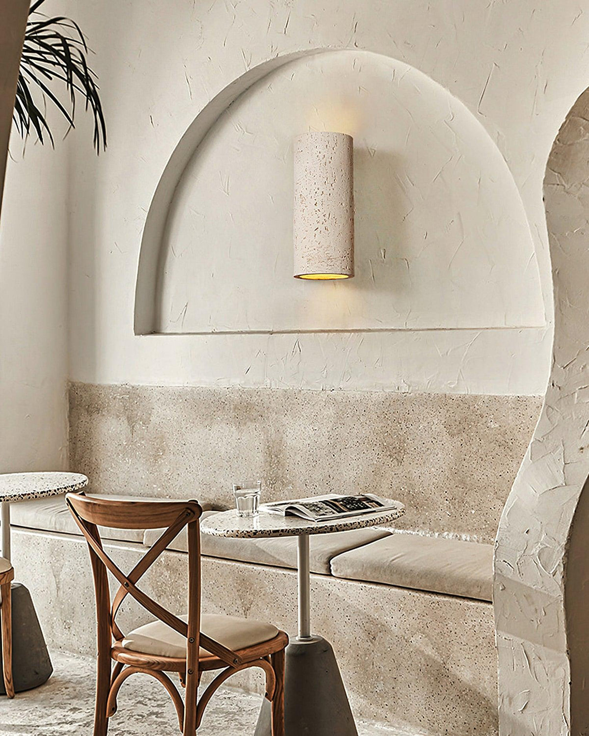 This Clérachic cylinder wall light sits inside a plastered arched niche above a café table and a cross-back chair.