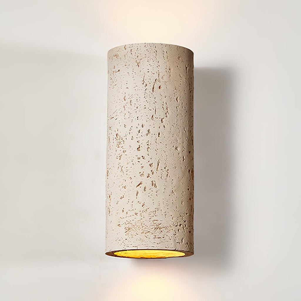 Close view of the cream cylinder, its pitted travertine-like surface and the golden inside edge of the open end; a Clérachic wall light.