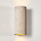 Close view of the cream cylinder, its pitted travertine-like surface and the golden inside edge of the open end; a Clérachic wall light.