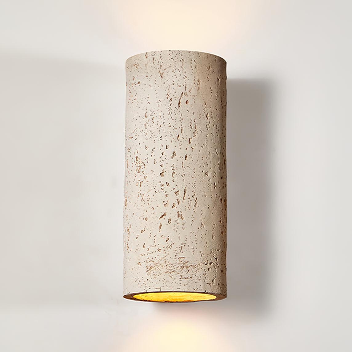 Close view of the cream cylinder, its pitted travertine-like surface and the golden inside edge of the open end; a Clérachic wall light.