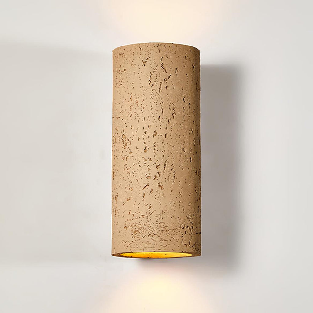 Close view of the tan cylinder wall light, its pitted surface and warm light at the base, against a pale wall; a Clérachic design.