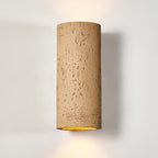 Close view of the tan cylinder wall light, its pitted surface and warm light at the base, against a pale wall; a Clérachic design.