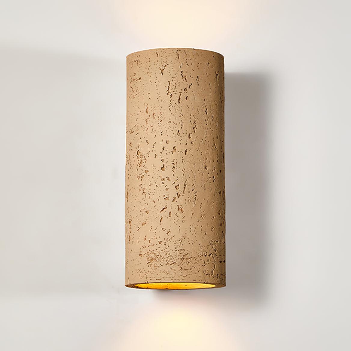 Close view of the tan cylinder wall light, its pitted surface and warm light at the base, against a pale wall; a Clérachic design.