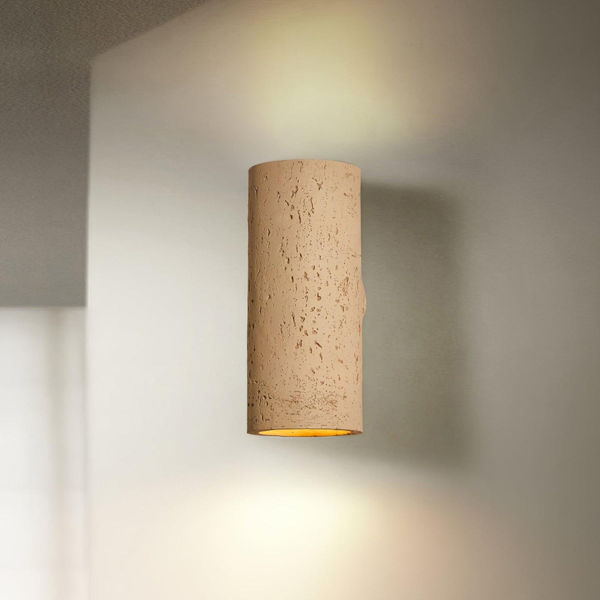 Tan cylinder wall light lit up and down, with a soft beam on the pale wall around it; a Clérachic wall sconce.