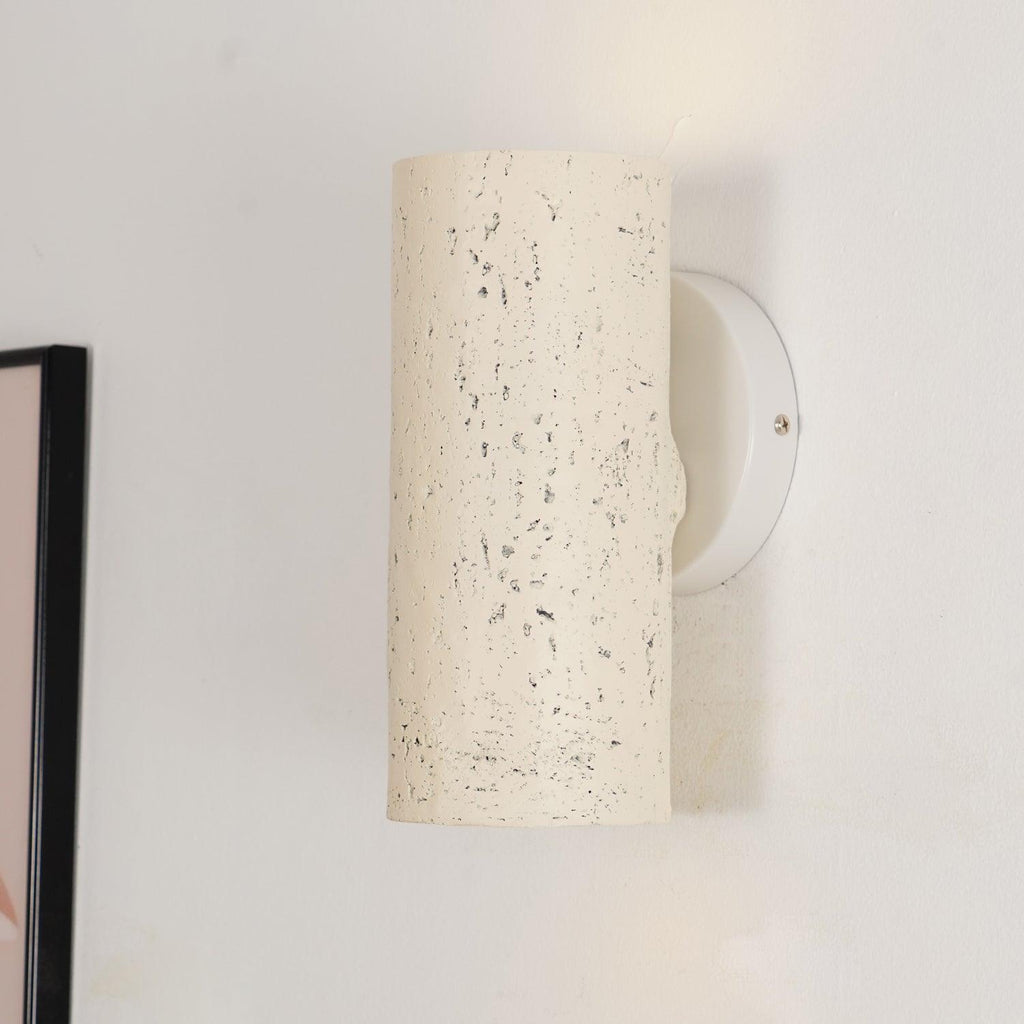 Close view of the cream cylinder's speckled surface and its round white wall plate with a screw; a Clérachic wall light.