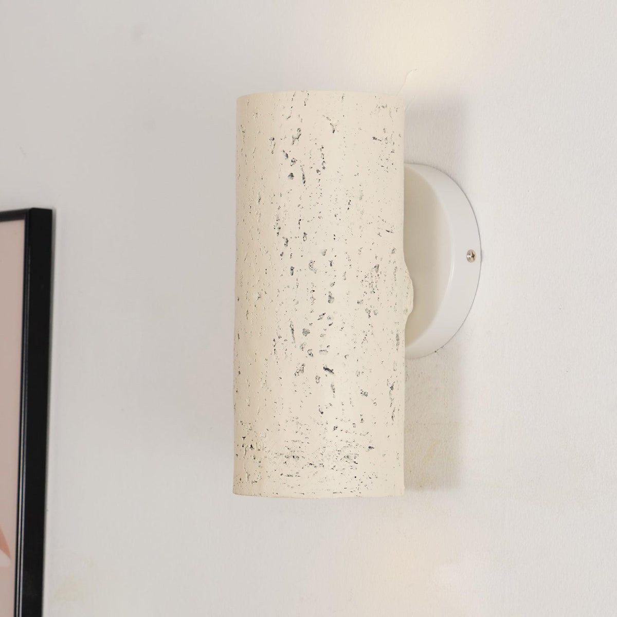 Close view of the cream cylinder's speckled surface and its round white wall plate with a screw; a Clérachic wall light.