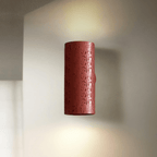 A red cylinder wall light with a pitted finish glows up and down against a pale wall; a Clérachic wall sconce.