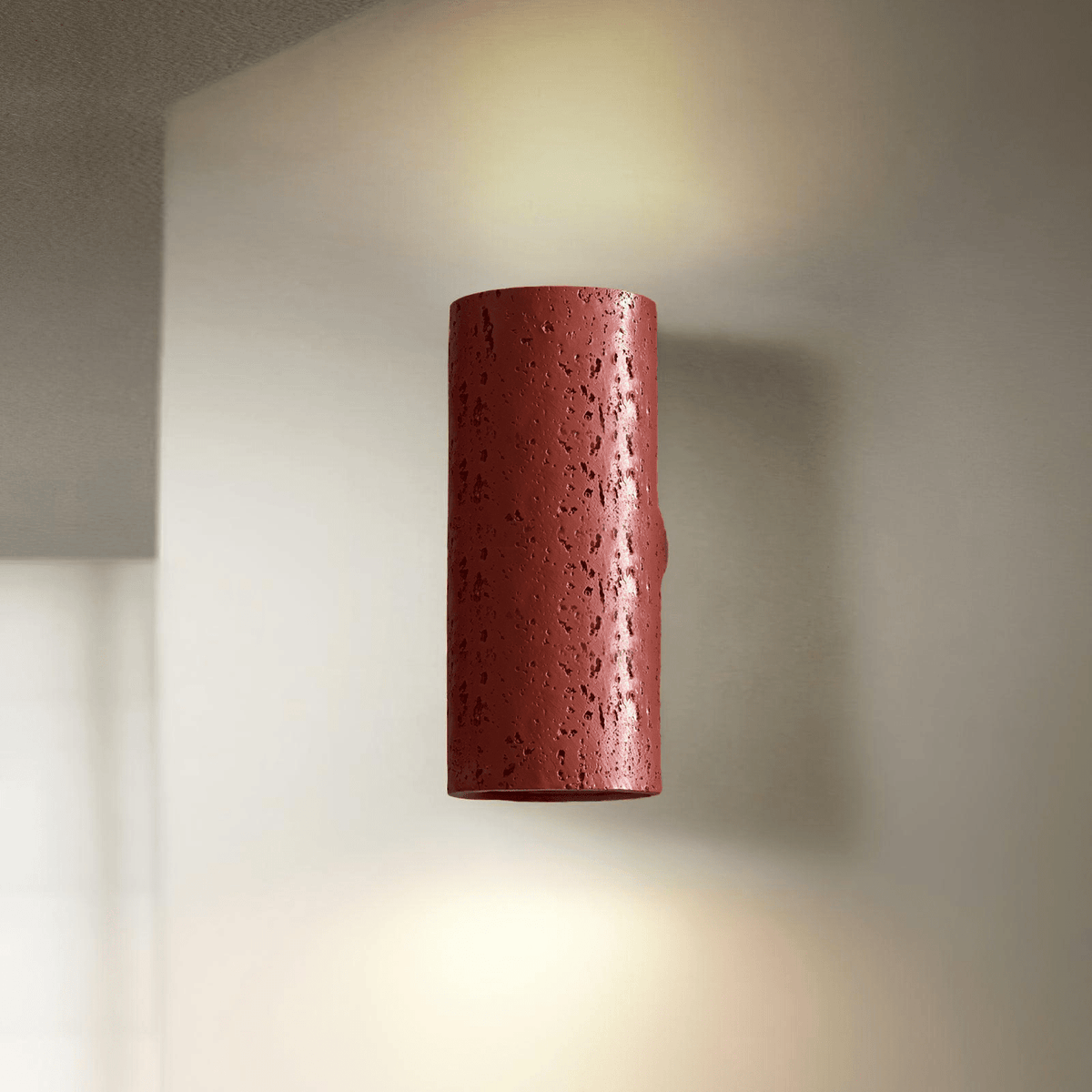 A red cylinder wall light with a pitted finish glows up and down against a pale wall; a Clérachic wall sconce.