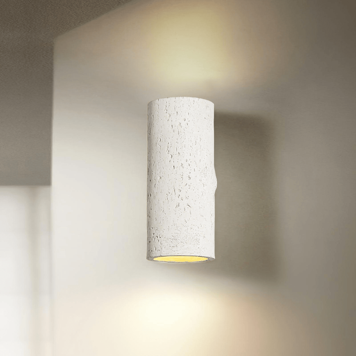 White cylinder wall light with a warm glow from the open lower end, and a wash of light on the wall above; from Clérachic.