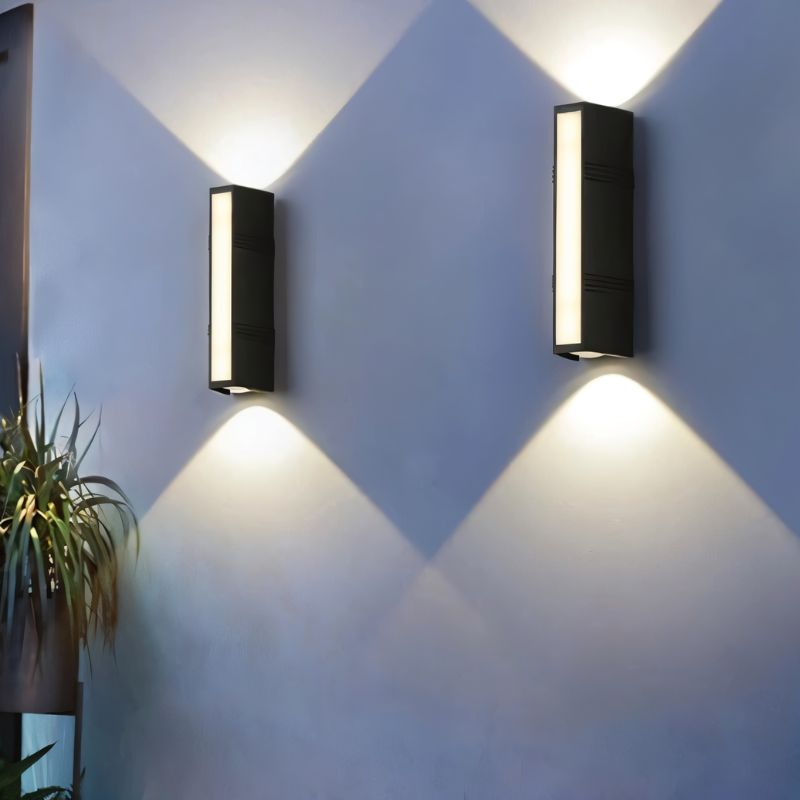 Clérachic pair of black rectangular wall lamps with side vents, casting crossing cool white beams on a pale grey wall.