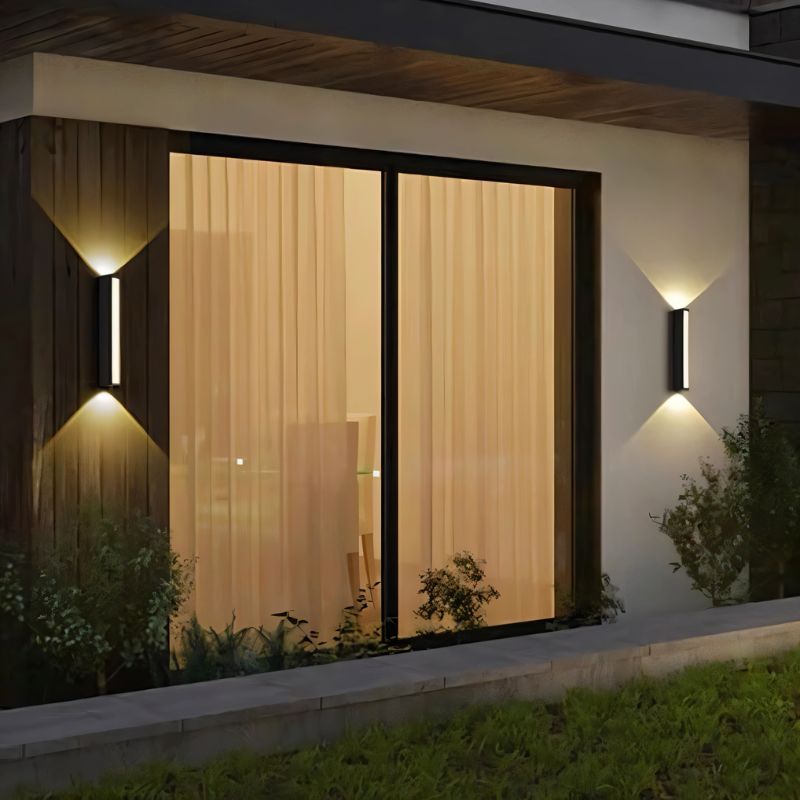 Clérachic two slim black wall lamps flanking a sliding patio door at night, each washing the cladding and render above and below.