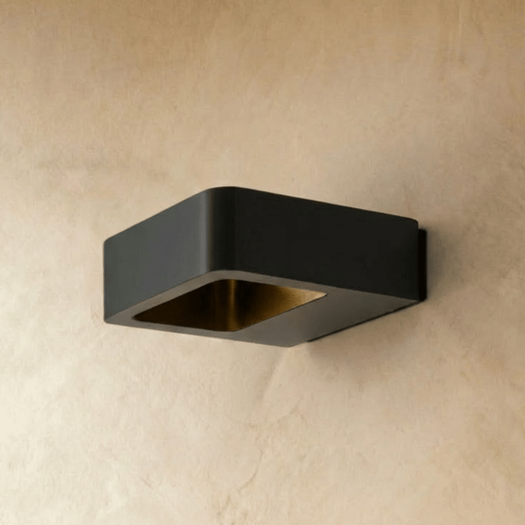 Clérachic square black wall light switched off, showing its brass-toned inner reflector on a warm plaster wall.