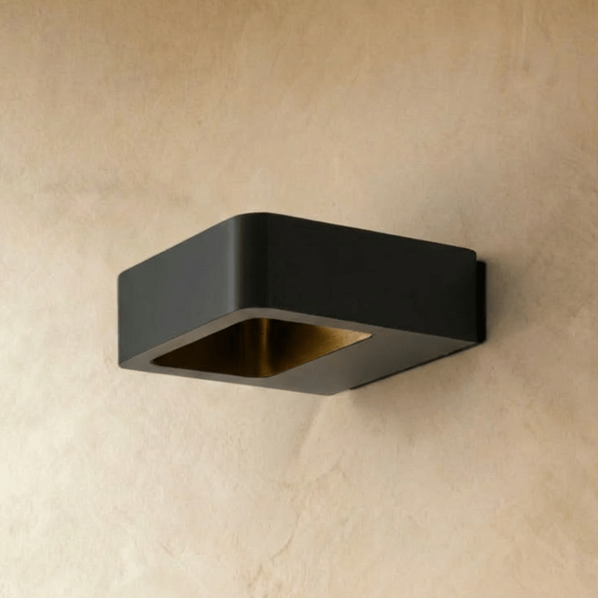 Clérachic square black wall light switched off, showing its brass-toned inner reflector on a warm plaster wall.